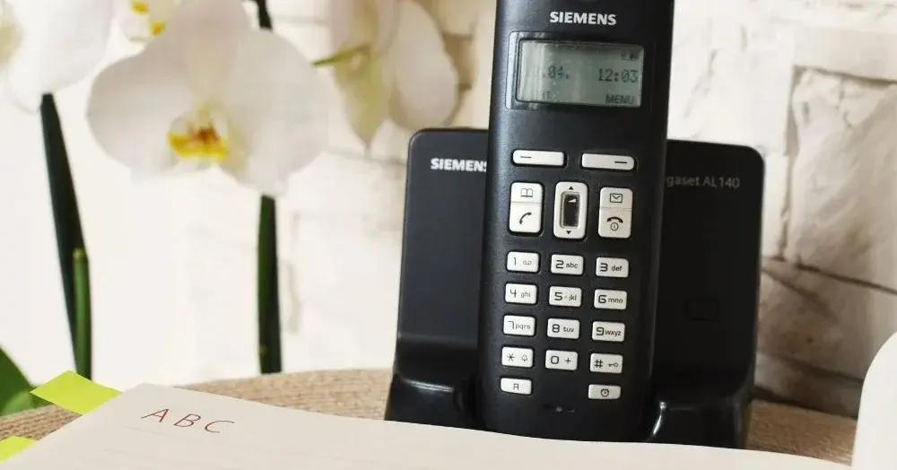 Konsolka drewniana ze storczykiem w tle, na niej czarny telefon