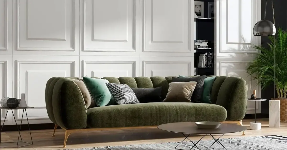 Oliwkowa kanapa z poduszkami na tle białej ściany w salonie