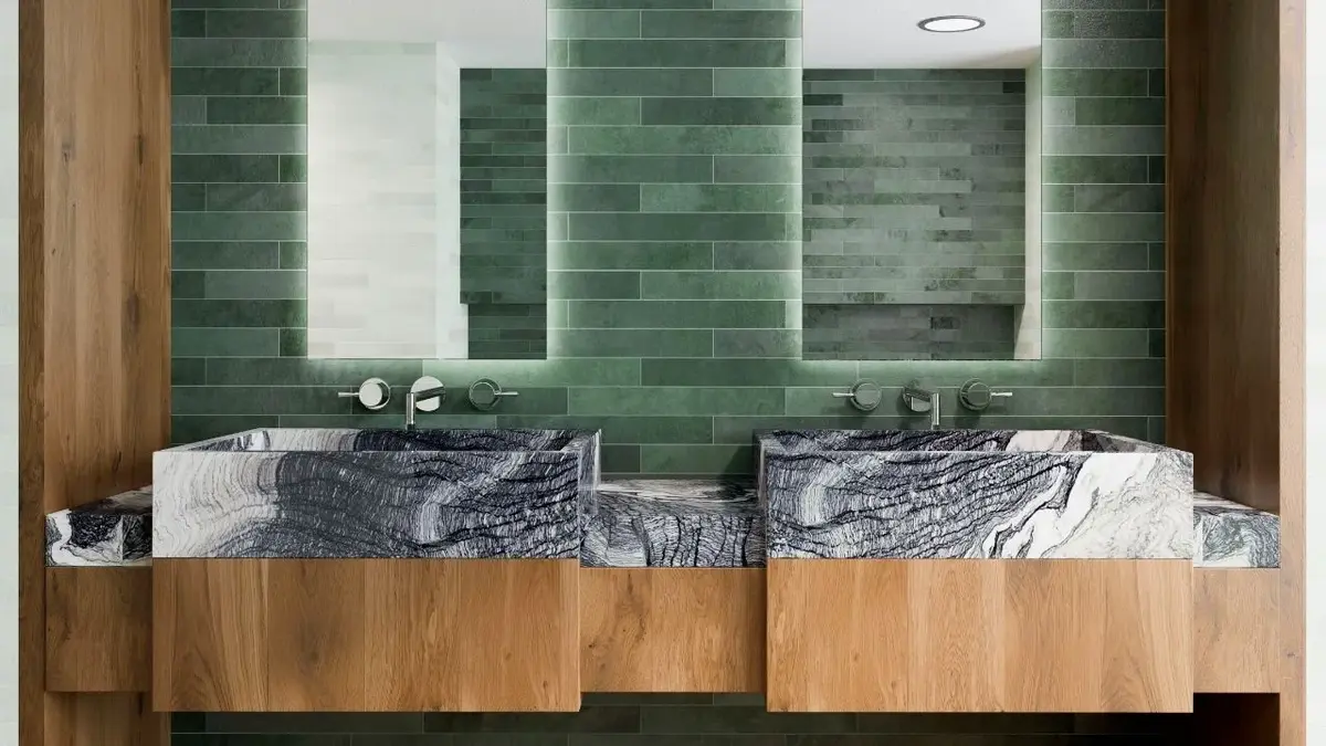 Łazienka z zielonymi, małymi kafelkami, kamiennymi umywalkami i drewnianymi szafkami