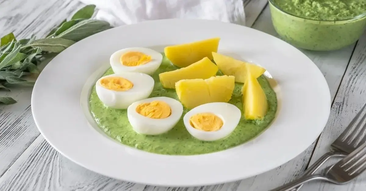 Jajka na twardo podane z zimnym zielonym sosem na białym talerzu.