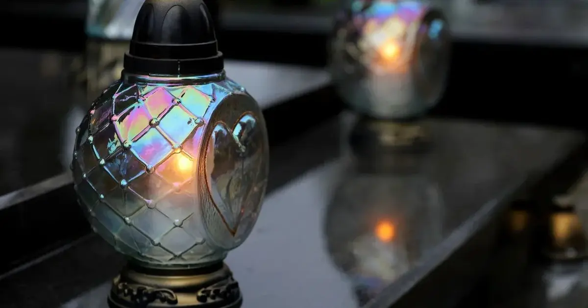 Zapalone znicze w szklanych osłonach ustawione na granitowej płycie grobowca