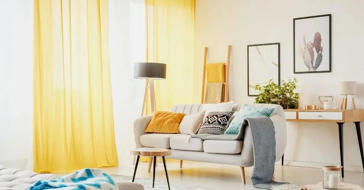 Przezroczyste żółte zasłony rozwiane przez wiatr w biało-szarym salonie