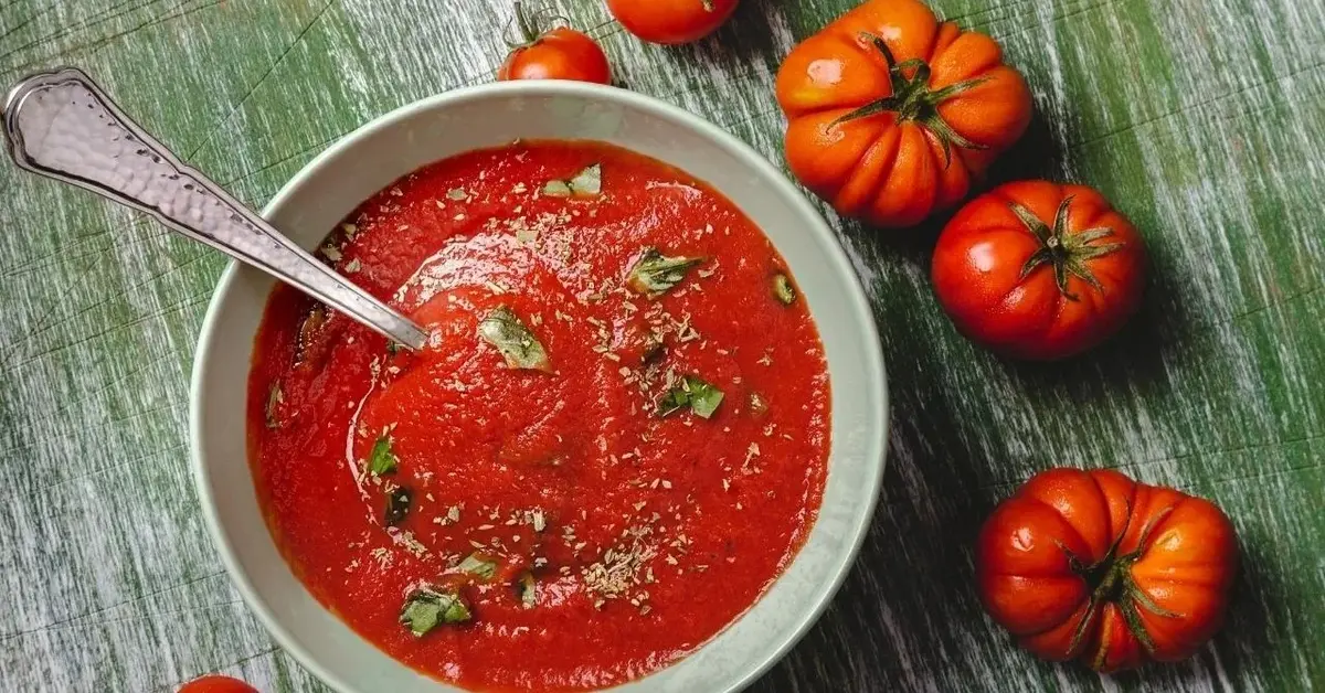 Zupa pomidorowa. Obok leżą pomidory.