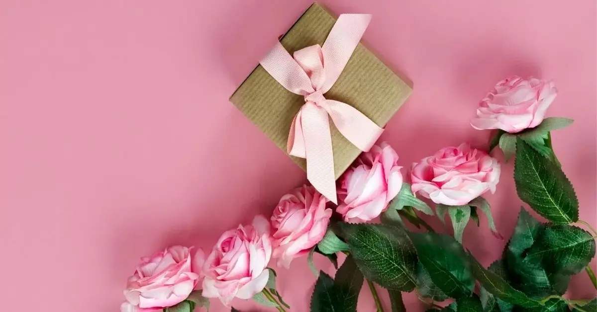 różowe róże na różowym tle obok szarego pudełeczka z różową wstążką