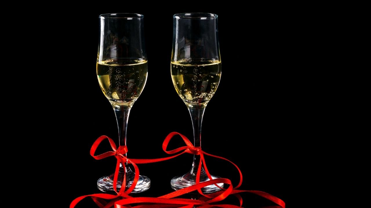 Dwa kieliszki z szampanem z nóżkami przewiązanymi czerwoną wstążką stoją na czarnym tle