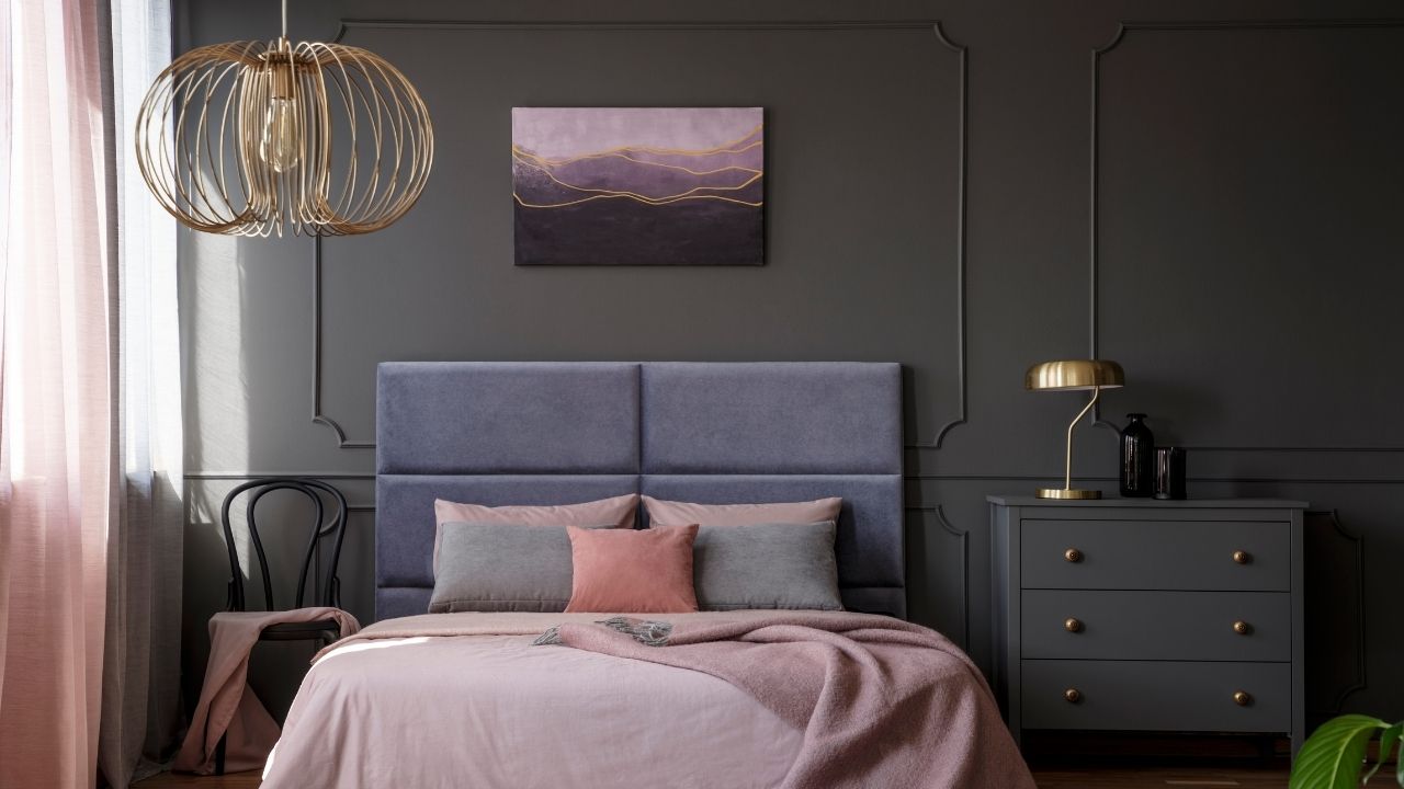 Wezgłowie tapicerowane welurową tkaniną w fioletowym kolorze nad łóżkiem z szaro-różową pościelą
